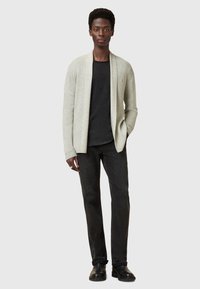Cardigan aperto grigio chiaro su una maglietta nera, abbinato a jeans scuri e stivali neri. Tessuto liscio, vestibilità rilassata, motivo a coste sottile nel tessuto.