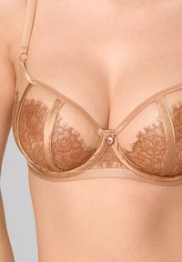 Koronkowy bralet w ciepłym beżowym odcieniu z wsparciem w postaci fiszbin, panelami z siateczki, dekoracyjnymi frędzlami i akcentem w postaci kryształka na środku. Regulowane ramiączka.