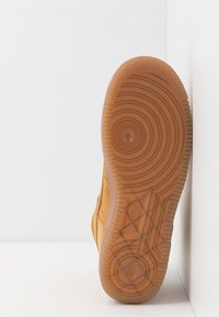 Tan mockasiner i mocka med rund gummisula. Texturerad yttersula med cirkulära och linjära mönster. Sido vy mot en enkel bakgrund.