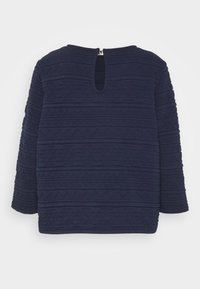 Dunkelblauer Pullover mit Dreiviertelärmeln, der ein strukturiertes Muster aus horizontalen Linien aufweist und eine Rückenöffnung mit Schlüsselöffnung sowie metallischen Beschlägen hat.