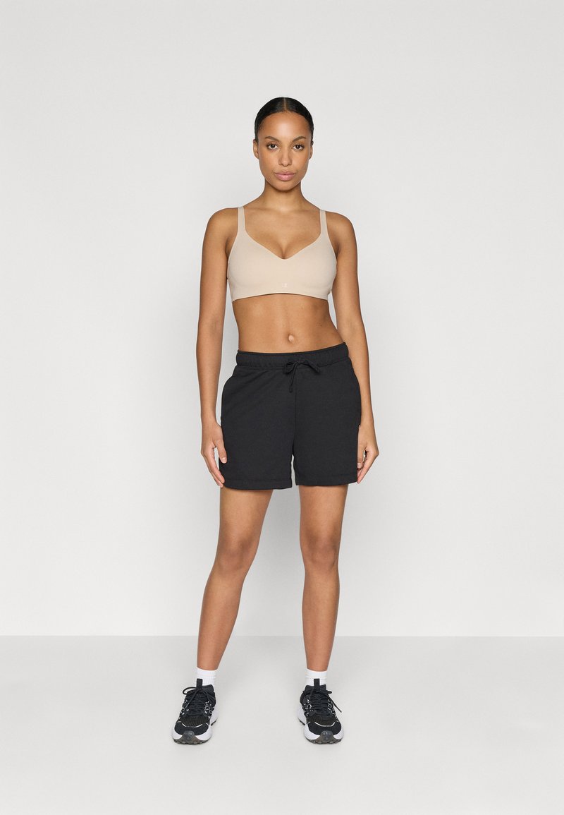 Reggiseno sportivo beige e pantaloni shorts neri. I pantaloni sono di lunghezza media, fino alla coscia, con una vita regolabile tramite cordoncino. L'outfit è abbinato a scarpe da ginnastica nere.