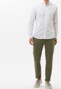 Biała koszula na guziki z długimi rękawami, zestawiona z podwiniętymi oliwkowozielonymi spodniami i jasnoszarymi trampkami. Prosty fason, bez wzorów.