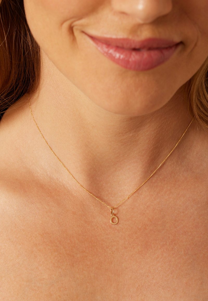 Gouden ketting met een dunne ketting en een cirkelvormige hanger, met een gladde afwerking. Het ontwerp is minimalistisch en elegant.