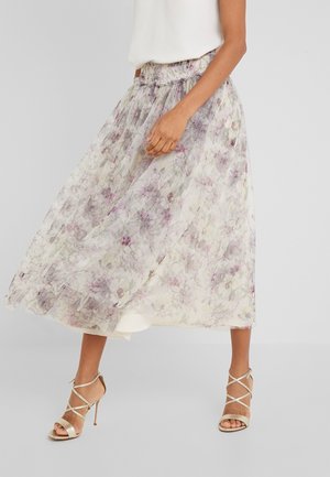 Maxirok met bloemenprint van doorschijnende, lichte stof met een gestrikte taille en tinten lavendel en groen; gecombineerd met sandalen met metallic bandjes.