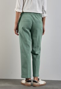 Pantalon en coton vert avec une coupe décontractée, taille élastique et deux poches arrière, associé à des baskets blanches avec des accents noirs.