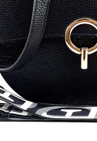 Zwarte leren tas met een textuur, voorzien van een gouden ronde hardwareaccent en een contrasterende strap met witte en grijze lettering.