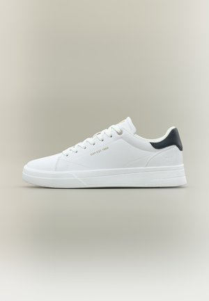 Sneaker bianca a taglio basso con lacci bianchi, linguetta posteriore nera e testo dorato "GAP EST. 1969" sul lato, su uno sfondo neutro.
