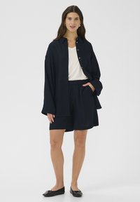 Navy button-up shirt, white top, navy shorts, and black flats. Lightweight fabric, loose fit, and elastic waistband on shorts.