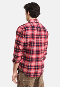 Czerwona i granatowa koszula w kratę z długimi rękawami, z zapięciem na guziki, z detalem plisy na piersi. Posiada zaokrąglony dół i podwinięte mankiety.