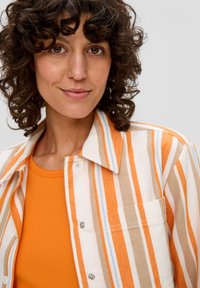 Gestreepte button-up shirt met oranje, beige en blauwe lijnen; lichte stof; met een zak; gedragen over een oranje tanktop.
