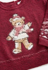 Roter Strickpullover mit einem Bärenmotiv in Braun und Weiß, der einen Schal trägt. Die Textur ist flauschig mit gerippten Bündchen und Saumdetails.