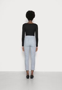 Top negro de manga larga con textura acanalada combinado con jeans ajustados de tiro alto en azul claro, con bolsillos traseros. Modelo lleva zapatos negros.