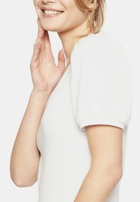 Biały prążkowany top z bufkami, wyróżniający się teksturowanym materiałem i dopasowanym krojem, podkreślający miękki, gładki wygląd.