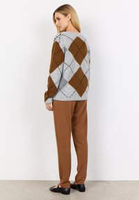 Maglione argyle grigio e marrone con tessuto strutturato, vestibilità ampia, abbinato a pantaloni marroni a taglio comodo e ballerine nere, visto da dietro.