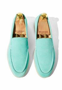 Mocasines de ante azul claro con una textura suave, costuras blancas y suela de goma. Se han insertado árboles de zapato de madera para mantener la forma.