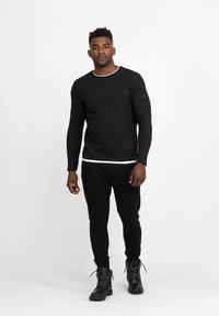 Maglione nero a coste con maniche lunghe e collo a giro bianco, abbinato a pantaloni neri attillati e stivali neri con lacci.