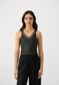 Schwarzes Satin-Camisole mit Spitzenbesatz am Ausschnitt, mit dünnen Trägern. Kombiniert mit schwarzen plissierten Hosen für eine schlanke Silhouette.