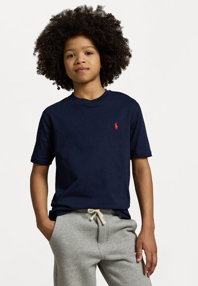 T-shirt en coton bleu marine avec un col rond et des manches courtes, arborant un petit logo rouge sur la poitrine, associé à un pantalon de jogging gris.
