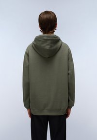 Sweatshirt vert olive avec une texture douce, dos sans caractère, capuche attachée et ourlet côtelé. Accessoires non visibles, design simple.