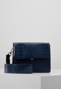 Borsa a tracolla blu navy con texture coccodrillo, dotata di chiusura a pattina, accessori in oro e una lunga tracolla regolabile.