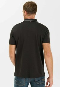 Zwarte poloshirt met een geribbelde kraag, contrasterende witte afwerking en korte mouwen. Glad materiaal en rechte zoom.