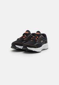 Zapatillas deportivas negras con parte superior de malla, acentos naranjas y suelas acolchadas. Presenta cordones y logotipo en la lengüeta. Suela texturizada para mayor agarre.
