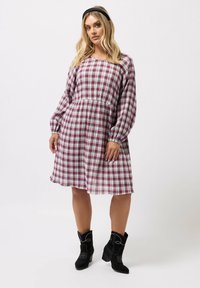 Punainen ja valkoinen ruudullinen mekko, jossa on pitkät hihat ja istuva vyötärö. Yhdistetty mustiin mokkanahkaisiin nilkkabootseihin, joissa on ompelemat yksityiskohtia.