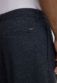 Donkergrijze wollen broek met een gestructureerde stof, rechte snit en een achterzak met een zwart label. Zacht, warm materiaal met subtiele patronen.