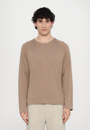 Brown long-sleeve sweatshirt with a crew neck and raglan sleeves, made from soft fabric. Paired with light-colored textured trousers.