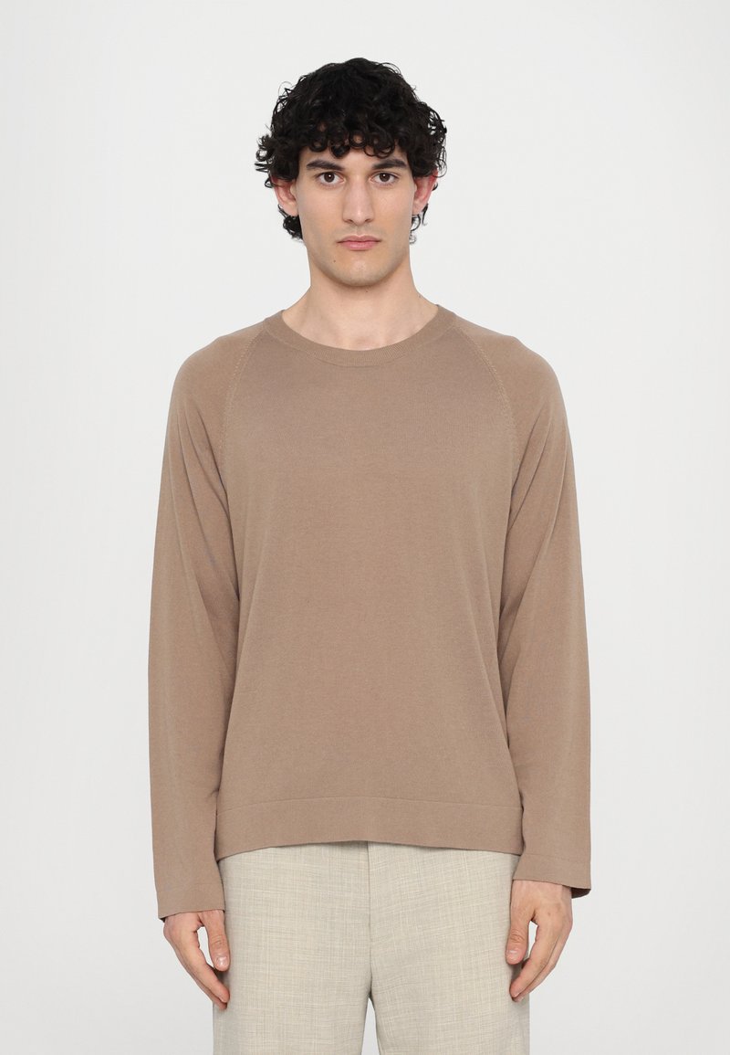 Brown long-sleeve sweatshirt with a crew neck and raglan sleeves, made from soft fabric. Paired with light-colored textured trousers.