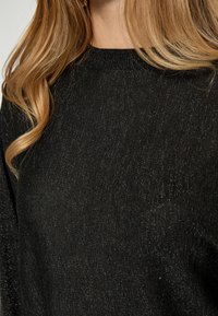 Black knit sweater with subtle metallic threads, round neckline, and soft texture. Features long sleeves and a relaxed fit.