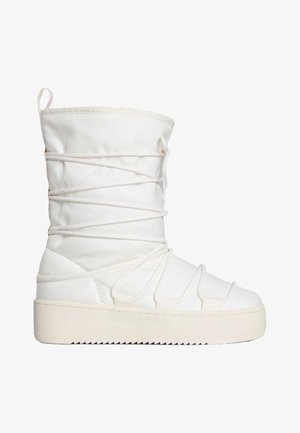 Stivale bianco imbottito con gambale alto, caratterizzato da cinghie elastiche incrociate e una suola platform spessa e texturizzata. Tessuto morbido e dettagli di accento.