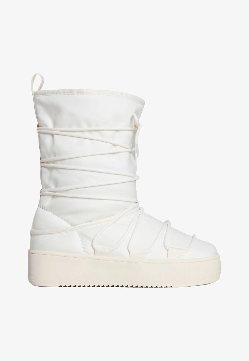 Stivale bianco imbottito con gambale alto, caratterizzato da cinghie elastiche incrociate e una suola platform spessa e texturizzata. Tessuto morbido e dettagli di accento.