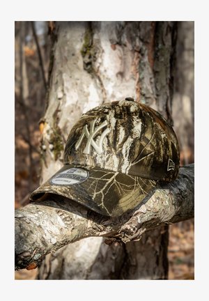 Camouflage baseball cap with a curved brim, featuring a raised light-colored New York logo, made of fabric with tree bark patterns.