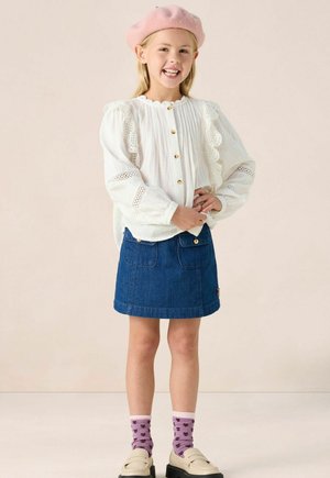 Blouse blanche avec des bords en dentelle et des boutons en or, assortie avec une jupe en jean, un béret rose et des chaussettes violettes à motif floral.