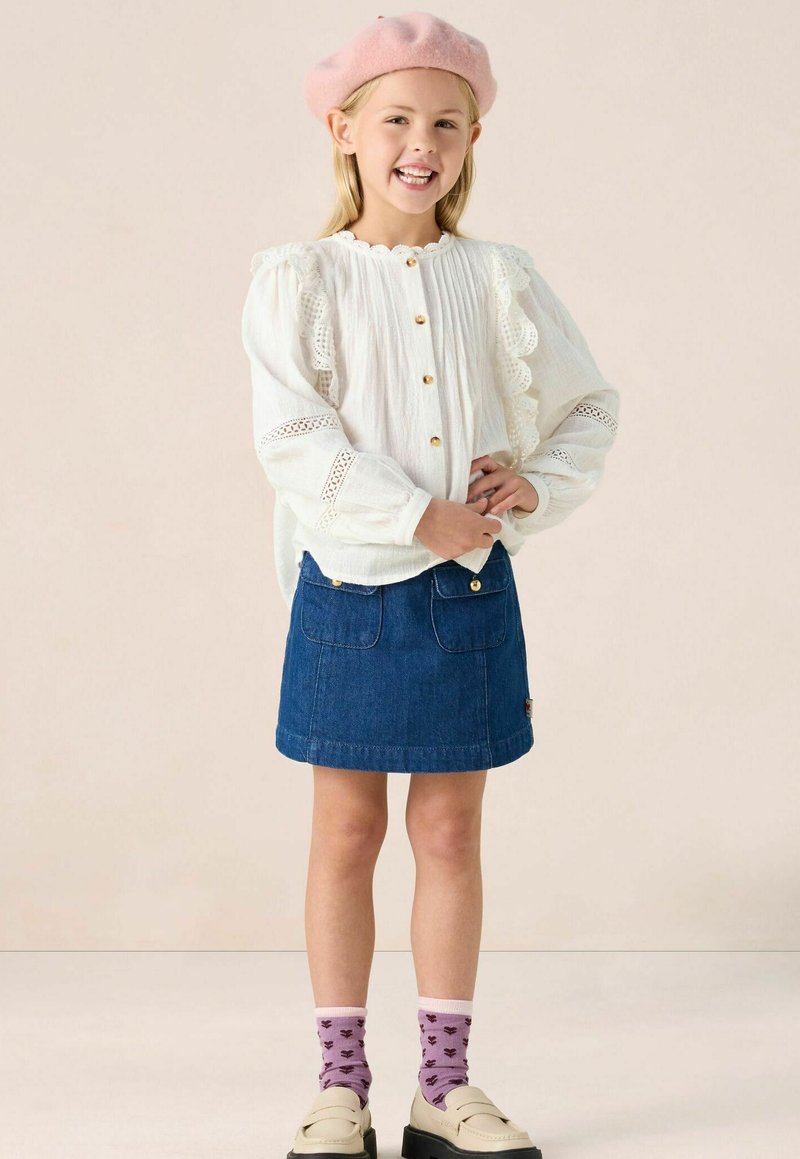 White blouse with lace edges and gold buttons, paired with a denim skirt, pink beret, and purple socks featuring a floral pattern.