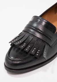 Mocassins en cuir noir avec un design à franges et de petites clous métalliques. Texture lisse, bout pointu et silhouette élancée.