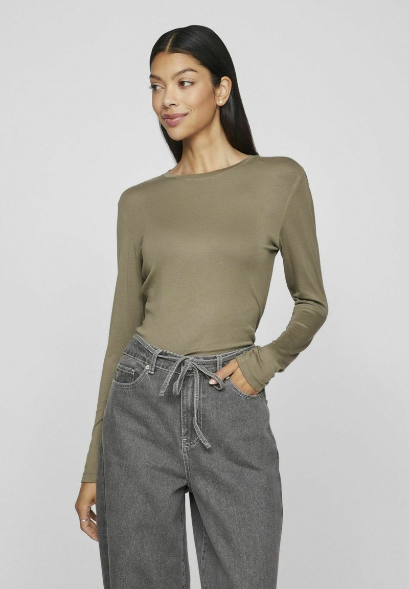 Olivgrön långärmad topp med rund halsringning och åtsittande ärmar, kombinerad med vida grå byxor med dragsko midja och sidofickor.