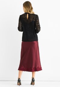 Black lace blouse with long sleeves and keyhole back detail, paired with a maroon satin skirt featuring a lace trim at the hem. Black heels.