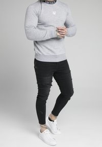 Grå sweatshirt med ribbade mudd, i kombination med svarta slim fit-jeans med slitna detaljer, och vita sneakers med guldaccenter.