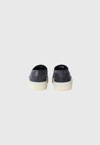 Pár tmavě šedých semišových slip-on bot s tlustými bílými podrážkami zobrazených ze zadní strany na jednoduchém světlém pozadí.