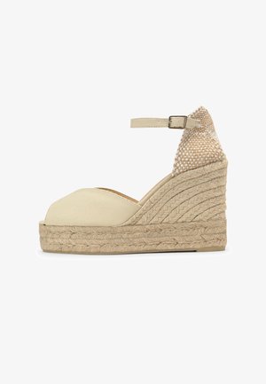 Sandalia espadrille beige con cuña, plataforma tejida, puntera abierta, tira en el tobillo y cierre de hebilla.