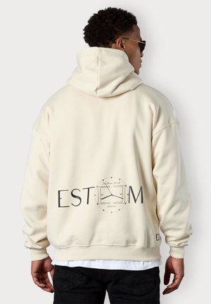 Cream-colored hoodie with a large graphic on the back that includes the word "ESTIM" and a circular clock design. Features a drawstring hood.