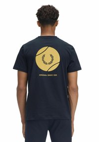 Camiseta de algodón azul marino que presenta un gran gráfico de una pelota de tenis amarilla con una corona de laurel y el texto "ORIGINAL DESDE 1952" en la parte de atrás.
