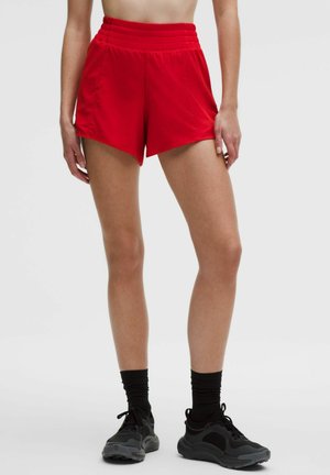Rode atletische korte broek met een hoge, geribbelde tailleband, met een losse pasvorm en een schuine zoomlijn. Gecombineerd met zwarte sportschoenen en sokken.