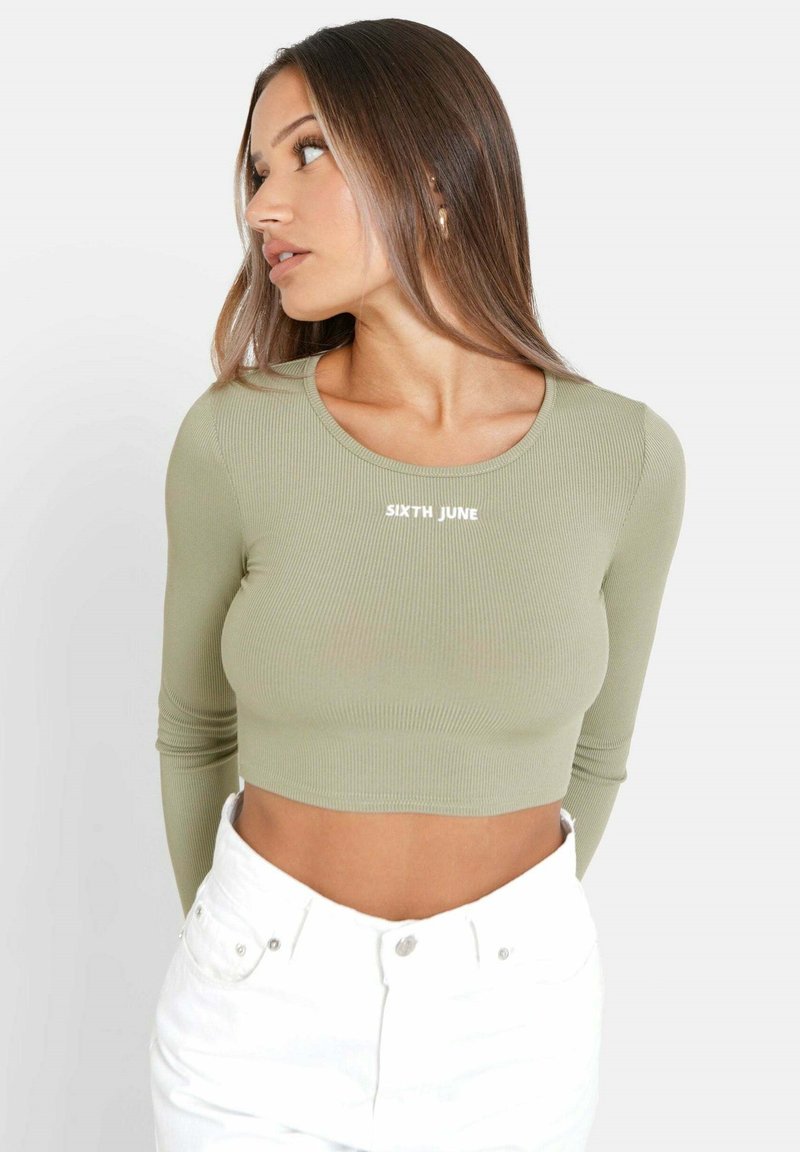 Olivgrön ribbat långärmad croptopp med rund halsringning och vit text "SIXTH JUNE". Matchas med högmidjade vita byxor.
