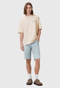 Beige oversize tričko s logem na prsou, světle modré džíny, bílé ponožky a hnědé nazouvací boty. Jednoduchý, neformální letní outfit.