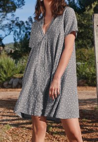 Robe en vichy noir et blanc avec un col en V, des manches courtes et une coupe ample qui s'évase à la taille. Tissu léger avec une texture subtile.