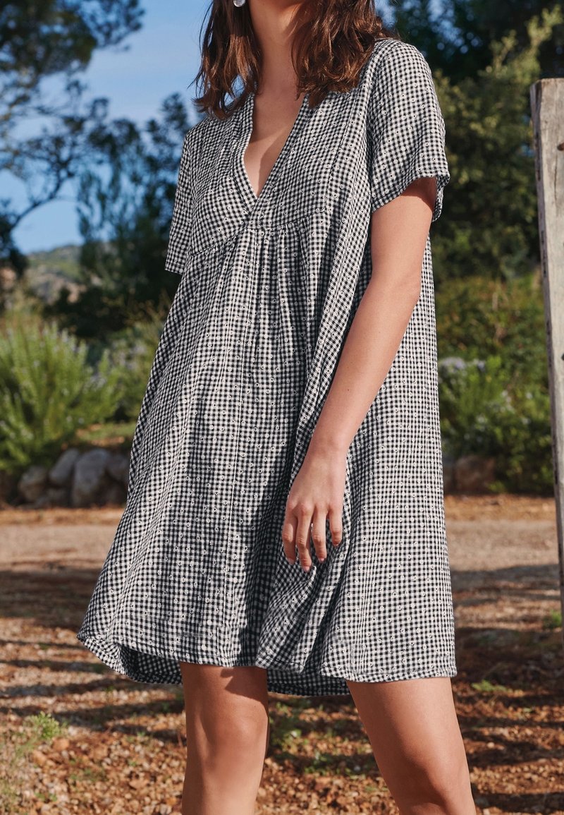 Robe en vichy noir et blanc avec un col en V, des manches courtes et une coupe ample qui s'évase à la taille. Tissu léger avec une texture subtile.