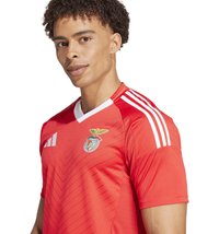 Rotes Fußballtrikot mit weißen Akzenten und drei Streifen auf den Schultern, mit einem Wappen auf der linken Brust und einem Chevron-Muster.